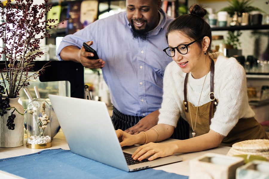Business Insurance - Business Owner Using Laptop on a Counter With Co-Owner Looking Over Shoulder and Smiling