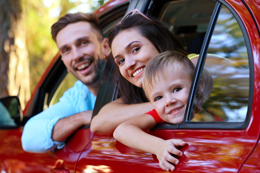 Personal Insurance - Happy Family with SonLooking Out the Window of a Red Car on a Sunny Day